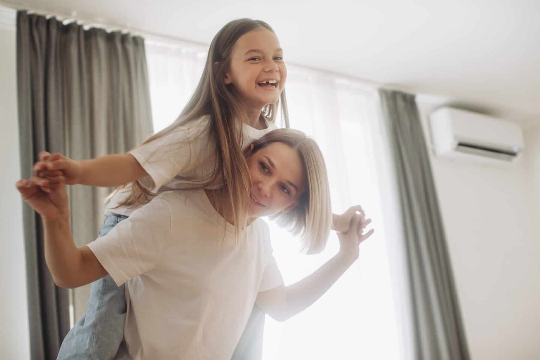 Happy mother piggybacking adorable little daughter at home.